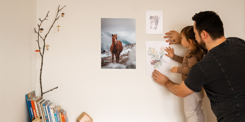 Mann hängt zusammen mit einem Kind ein Bild an die Wand